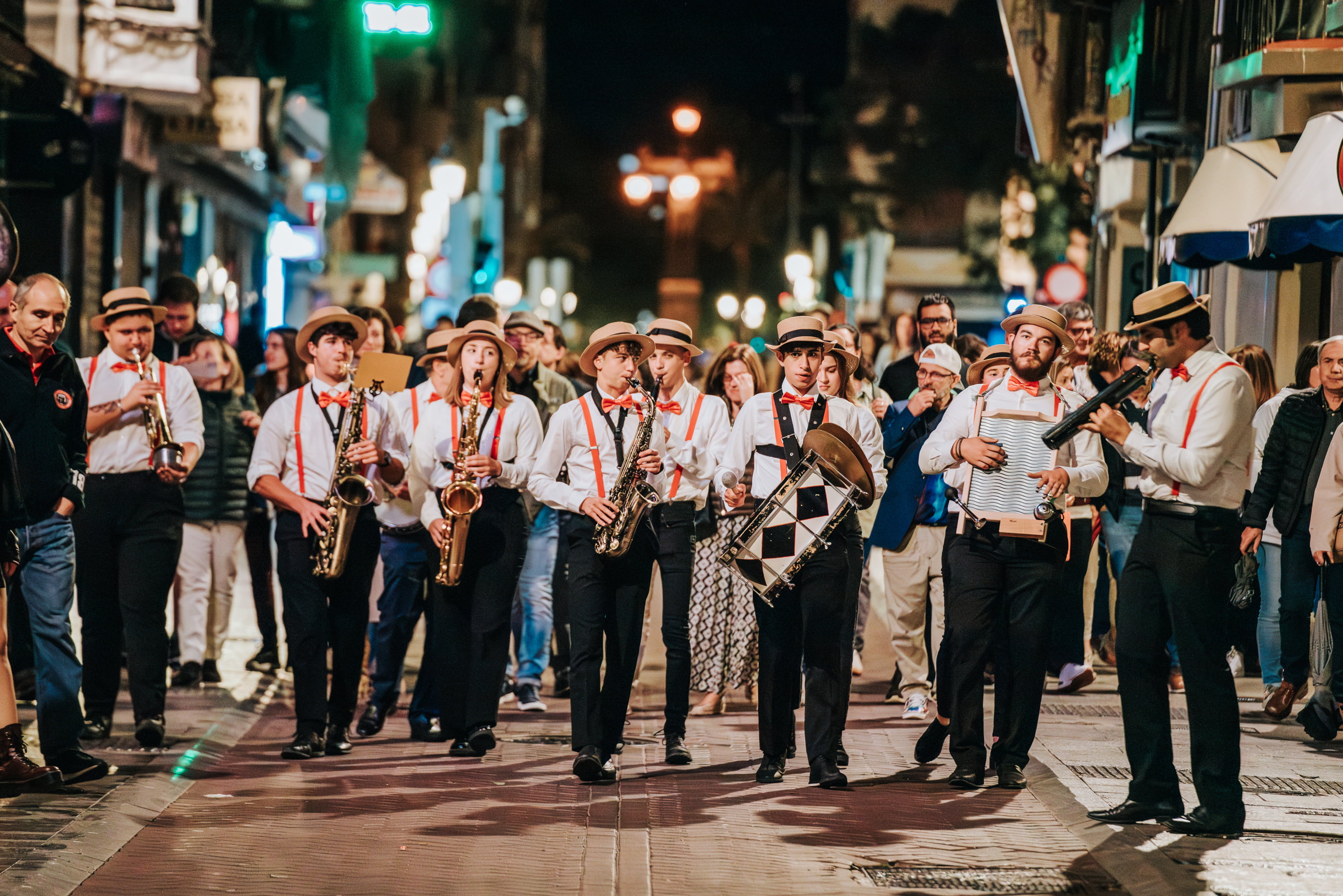músicos en la calle con sombreros de paja y tirantes y corbata rojas y pantalones negros y camisas blancas